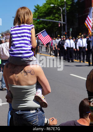 Middletown, CT USA. May 2018. Daughter sitting on mom`s shoulders waving flag during a Memorial Day celebration. Stock Photo